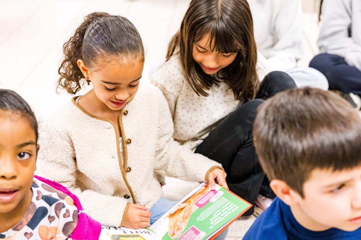 Two young girls reading together at a table during a youth mentorship program activity.